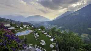 Un área de piscina con sillones y sombrillas, rodeada de exuberante vegetación y montañas al fondo.