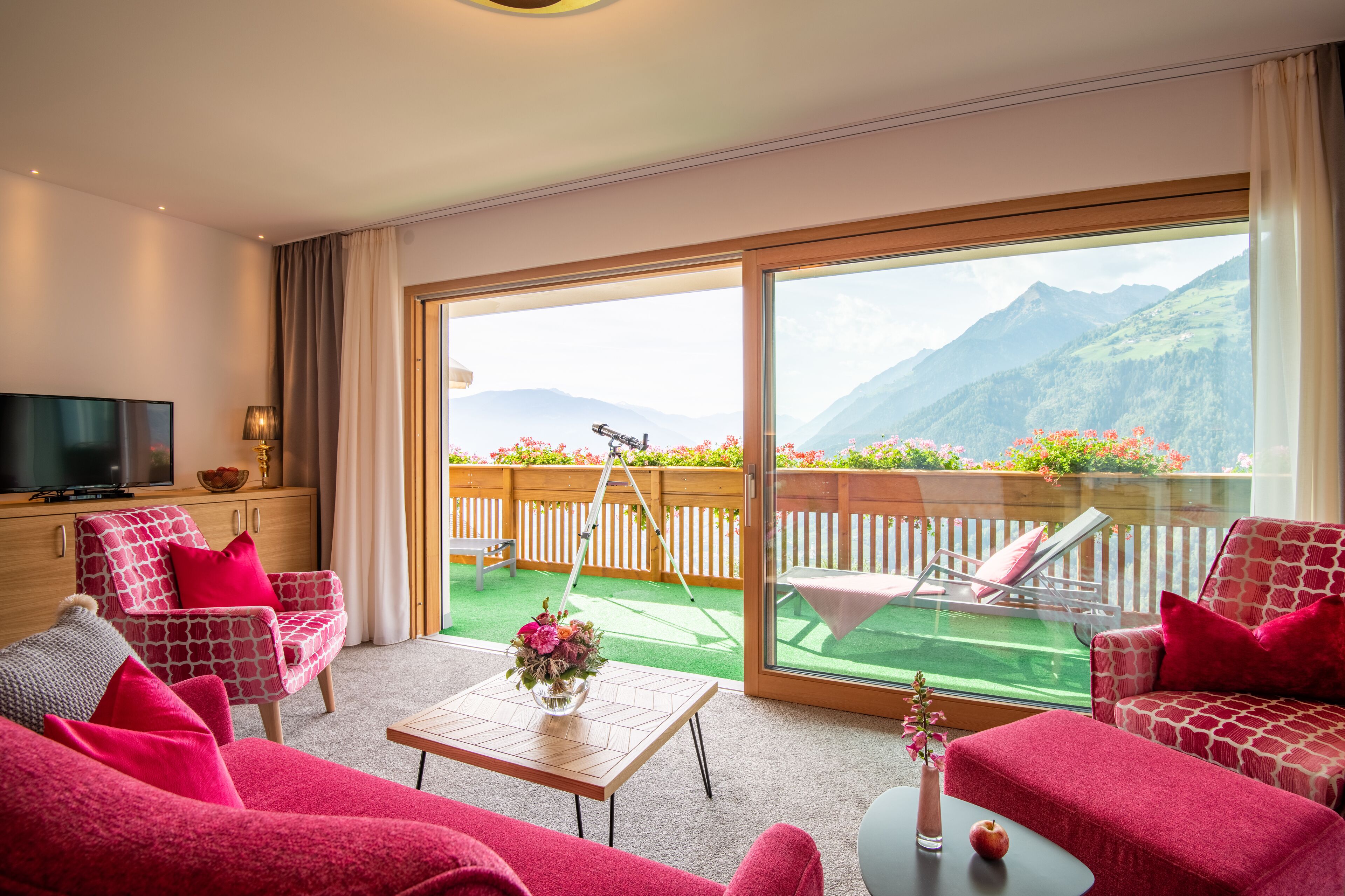 A hotel room with a balcony, a TV, a sofa, and a table with flowers.