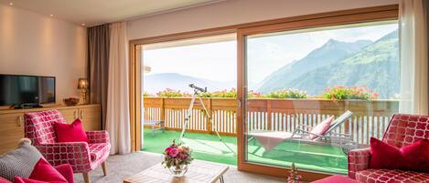 A hotel room with a balcony, a TV, a sofa, and a table with flowers.