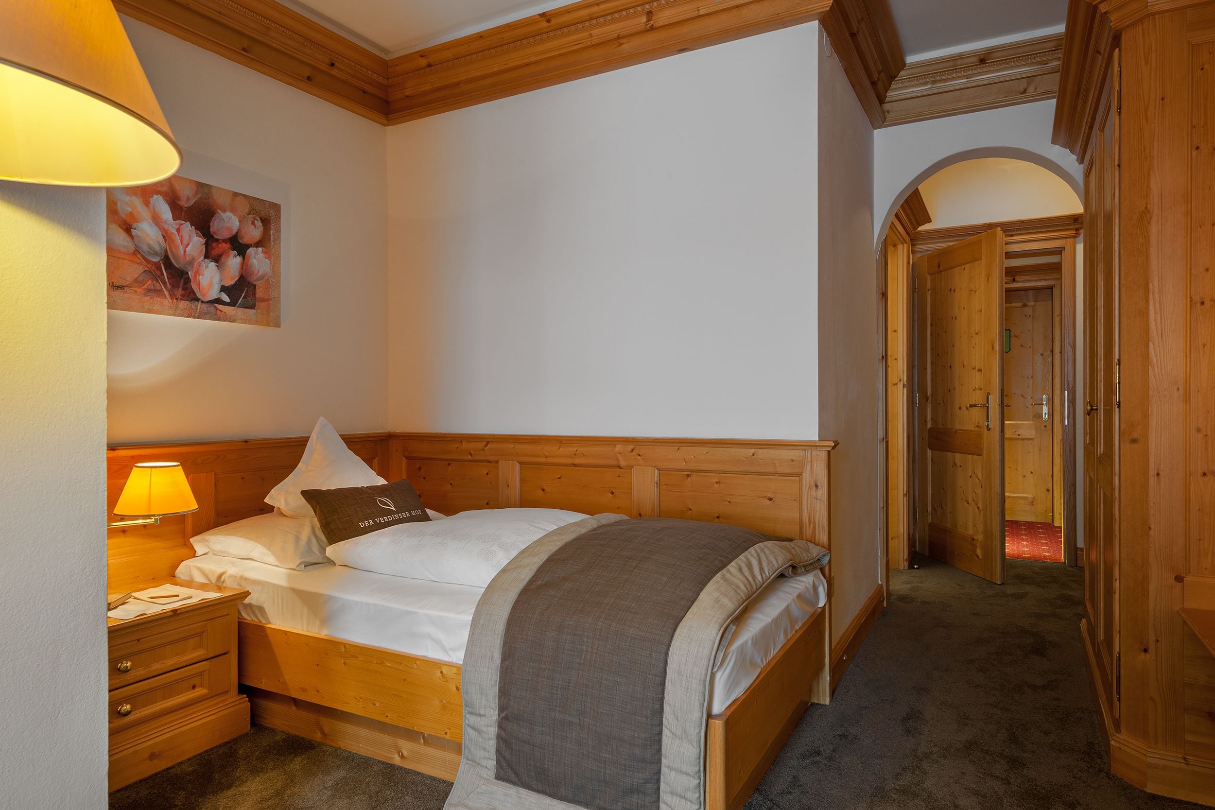 Ein ordentlich bezogenes Bett mit einem hölzernen Kopfteil, einer Nachttischlampe und einem Bild an der Wand.