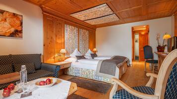 A cozy hotel room with a wooden ceiling, a bed with patterned bedding, a sofa, a dining table with apples, and a chair.
