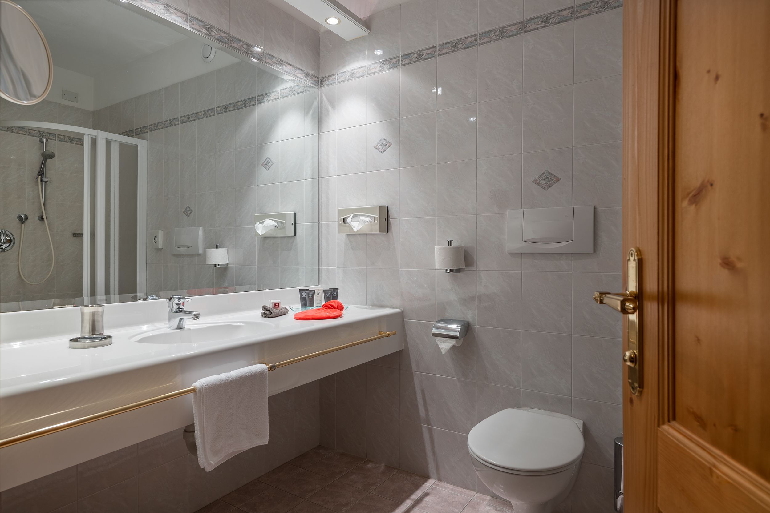 A modern bathroom with a large mirror, a sink with a towel rack, a toilet, and a shower area.