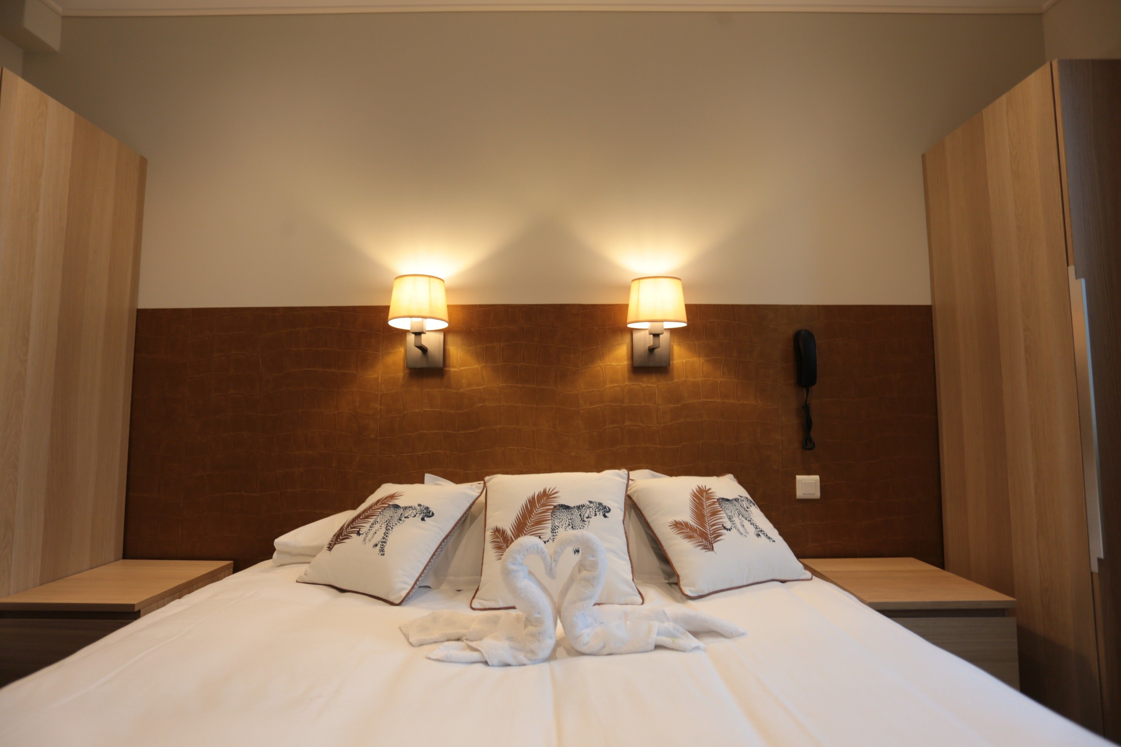 Une chambre d’hôtel avec un lit, deux lampes fixées au mur, un téléphone et des coussins décoratifs.