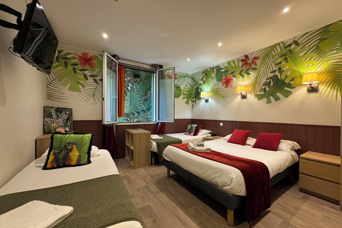 A hotel room with two beds, a TV, a window with curtains, and tropical-themed wall art.