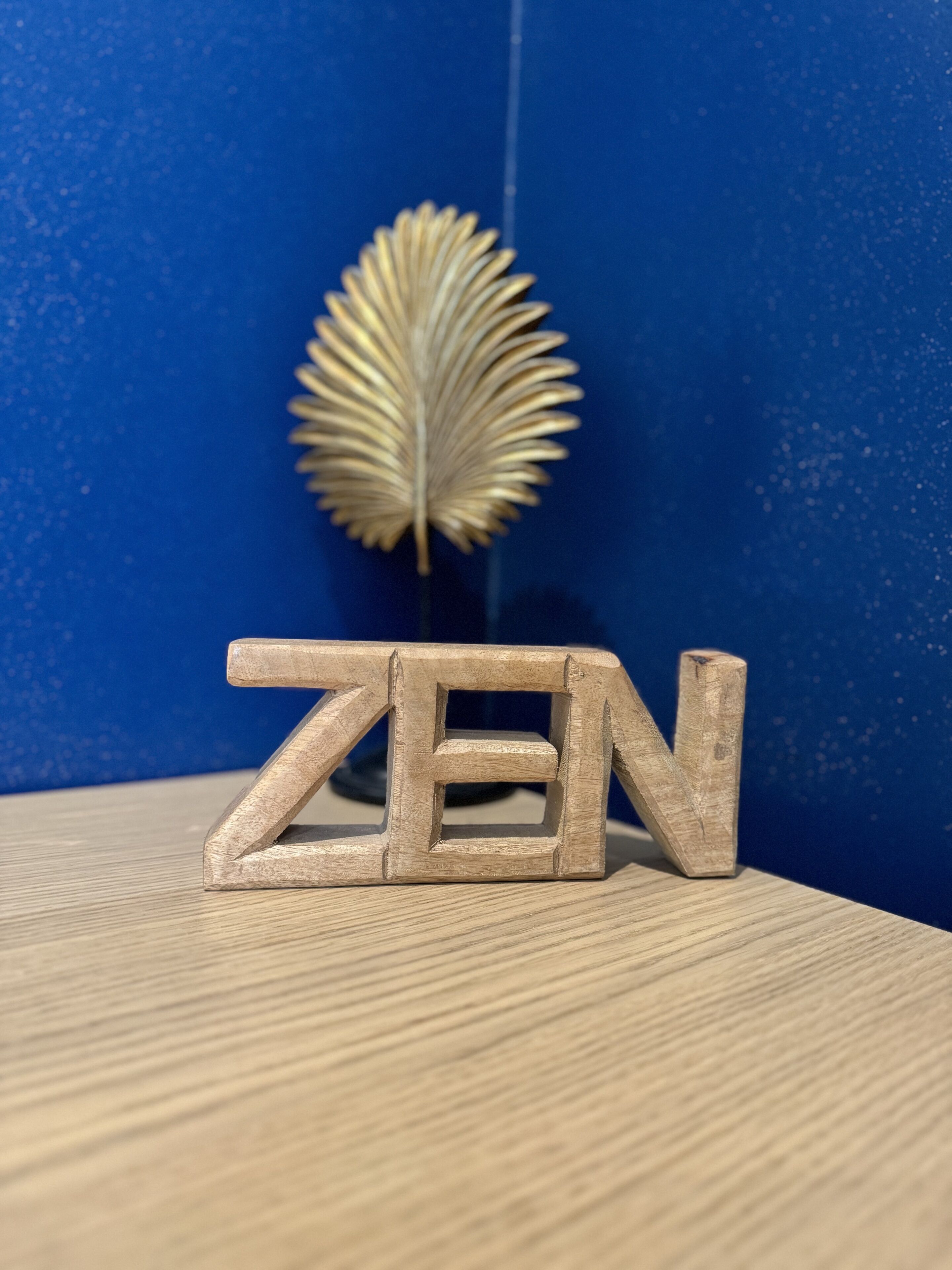 Wooden letters spelling "ZEN" on a wooden surface with a blue background and a decorative feather.