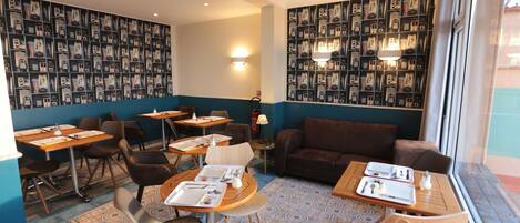 A restaurant with tables and chairs, a sofa, and a wall with framed pictures.
