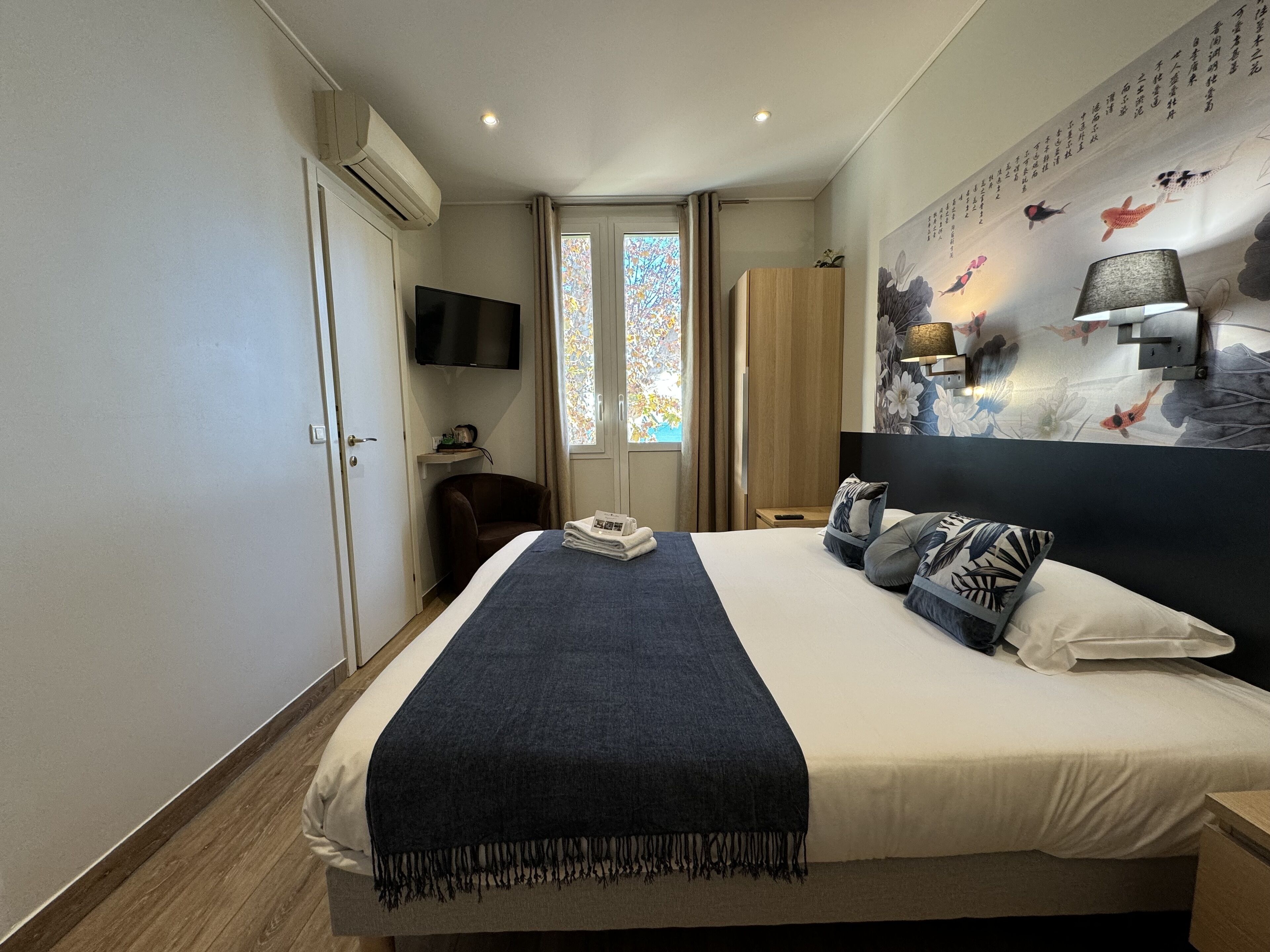 Habitación de hotel con una cama grande, un televisor de pantalla plana montado en la pared, una ventana con cortinas y una pared decorativa con motivos de peces.