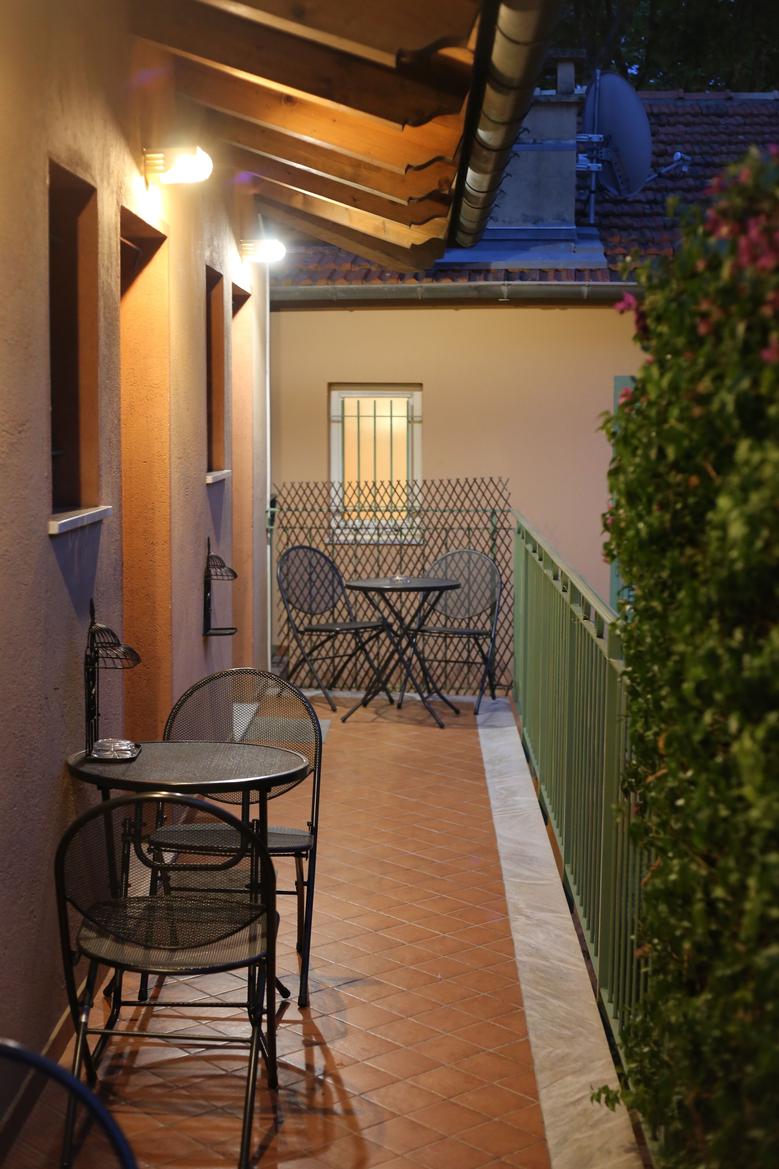 An outdoor patio with a table and chairs, a window, and a green fence.