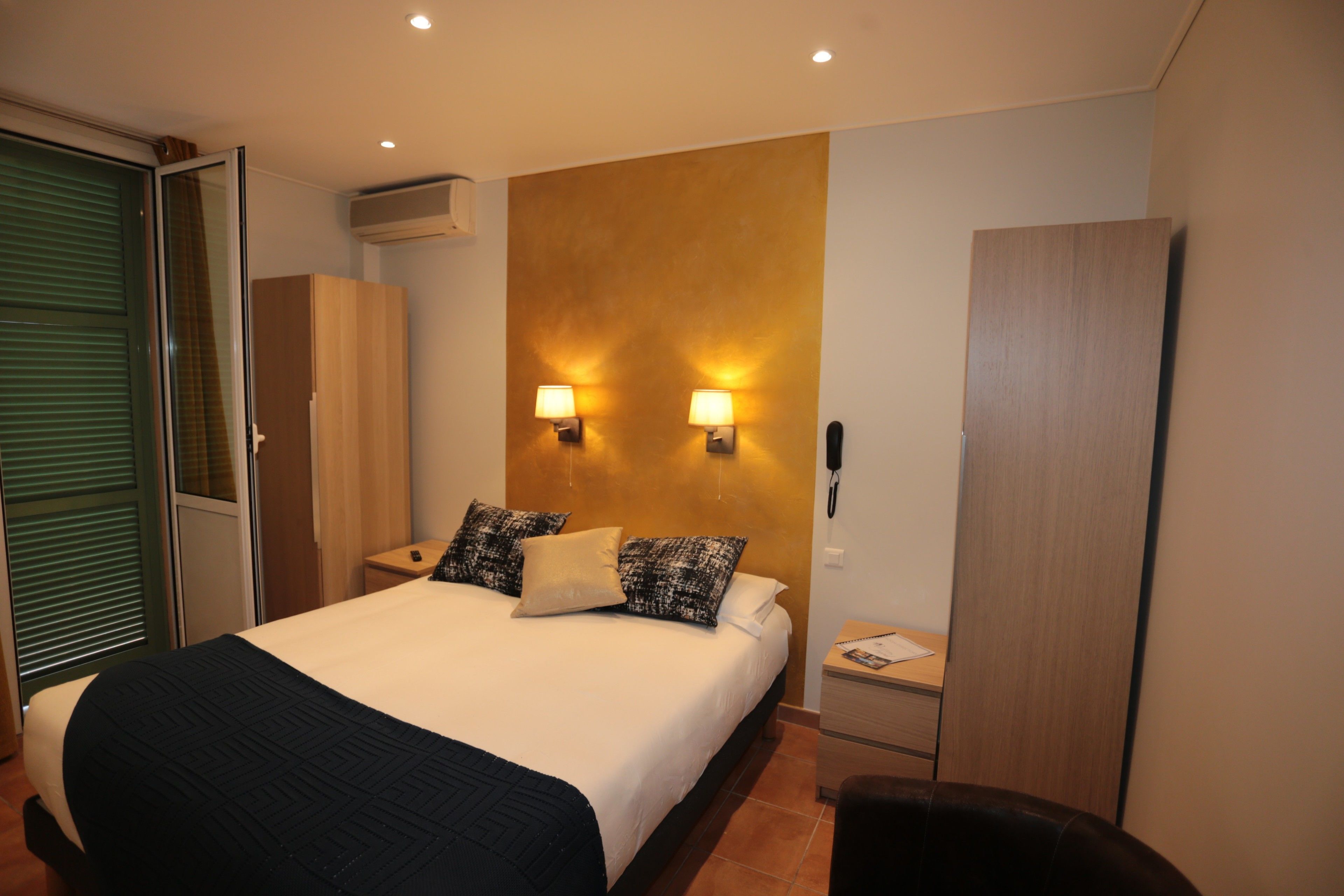 A hotel room with a bed, bedside tables, a wardrobe, and a sliding door.
