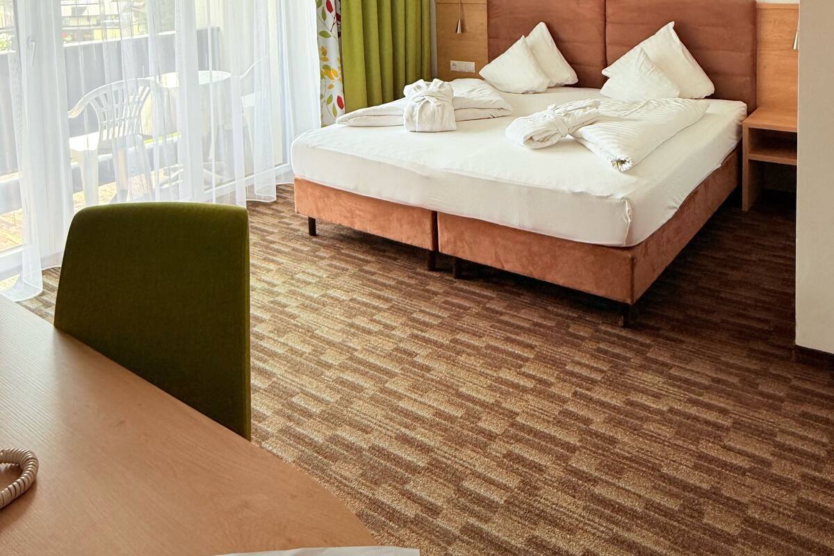A hotel room with a bed, a table, a chair, a lamp, and a picture on the wall.