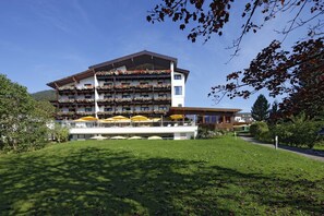 A multi-story hotel with balconies adorned with flowers, outdoor seating with yellow umbrellas, and a well-maintained lawn. - Achentalerhof (Achenkirch)