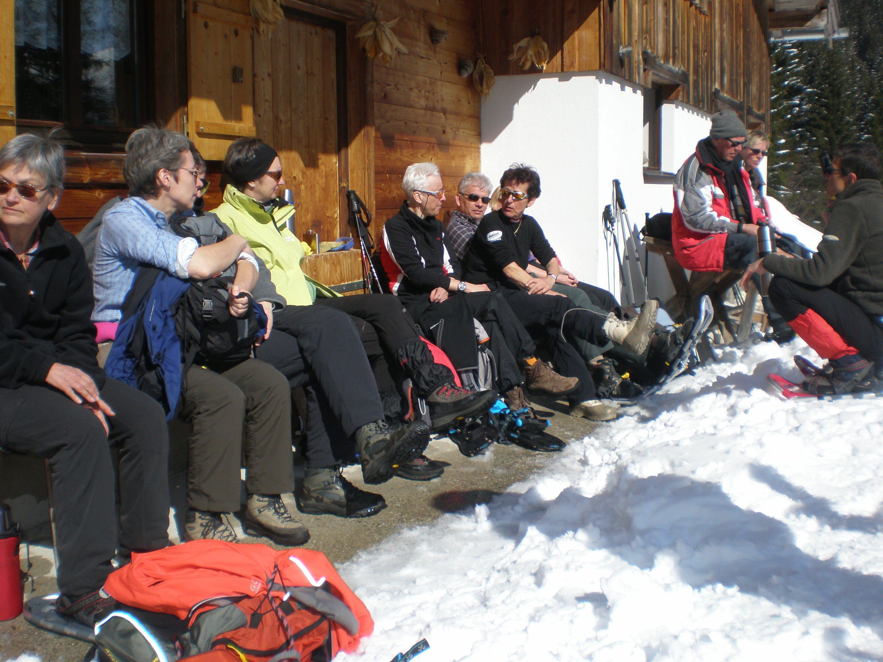 A group of people sitting outdoors in a snowy environment, possibly at a lodge or cabin.