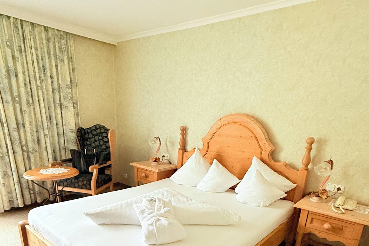 A neatly made bed with white linens and pillows, a wooden headboard, and a bedside table with a lamp and a telephone.
