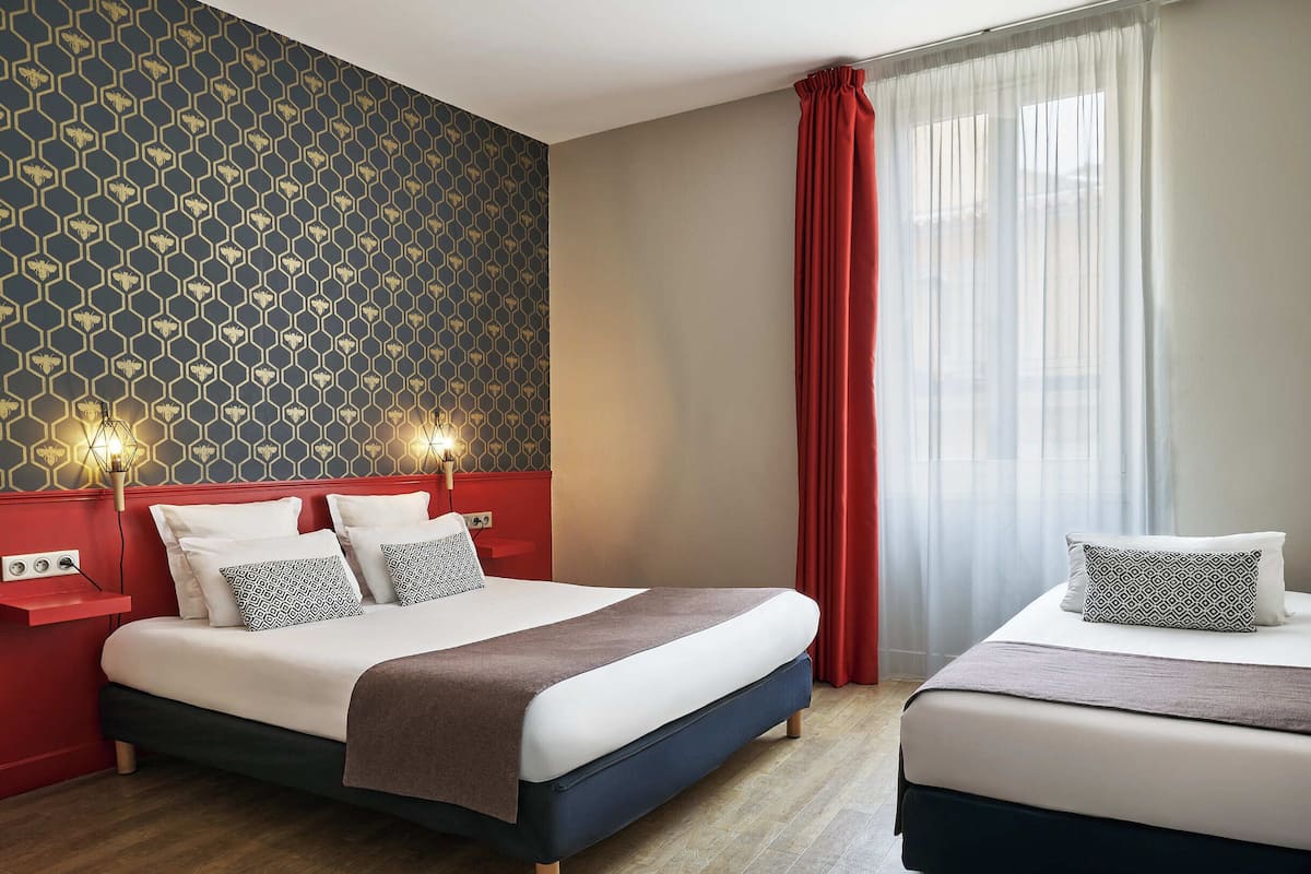Ein Hotelzimmer mit einem Bett, einem zusätzlichen Bett, einer roten Wand und einer Wand mit Muster.