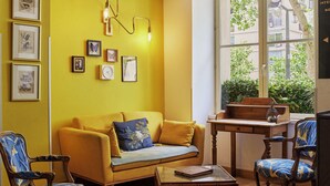 A room with a yellow wall, a sofa, two chairs, a table, and a window with a view of greenery. - Hôtel Marsiho by Happyculture (Marseille)