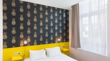 Une chambre d’hôtel avec un lit, une tête de lit jaune et un papier peint à motifs d’ananas.