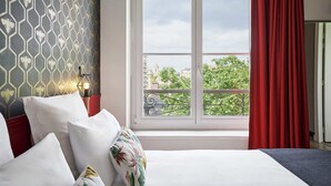 A hotel room with a bed, a window with a red curtain, a view of the city, and a patterned wall. - Hôtel Marsiho by Happyculture (Marseille)