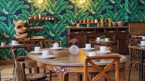 A dining area with wooden tables and chairs, a central decorative vase, and a wall with a leafy pattern. - Hôtel Marsiho by Happyculture (Marseille)