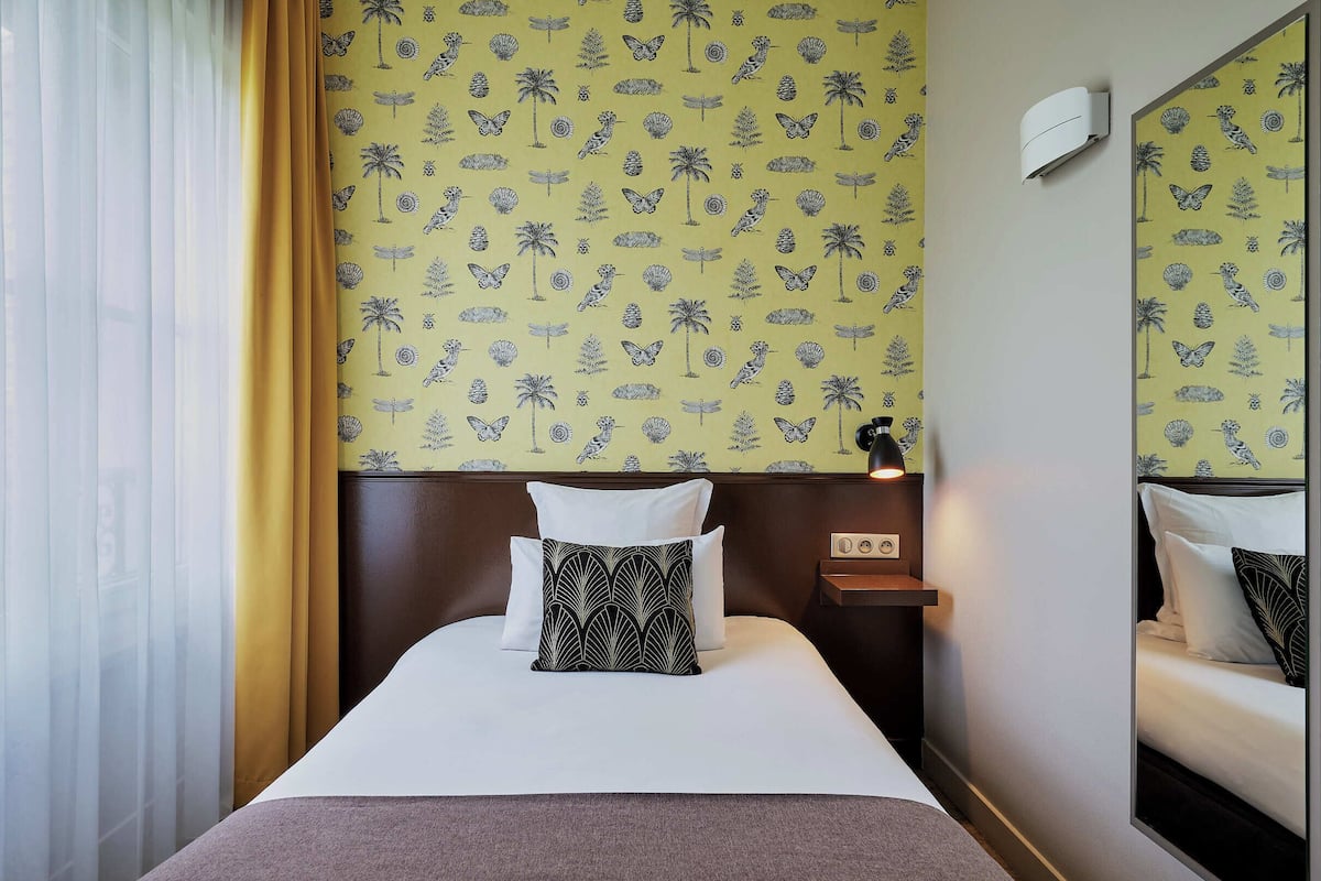 Ein Hotelzimmer mit einem Bett, einem Nachttisch, einem Spiegel und einer Wand mit tropischem Muster.