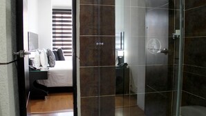 A hotel room with a bed, bedside table, and a bathroom with a glass shower enclosure. - Hotel Santafe Real (Bogotá)