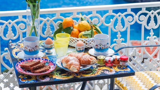 A table set with breakfast items, a vase with yellow flowers, and a view of the sea. - B&B Casa Nilde Positano (Positano)