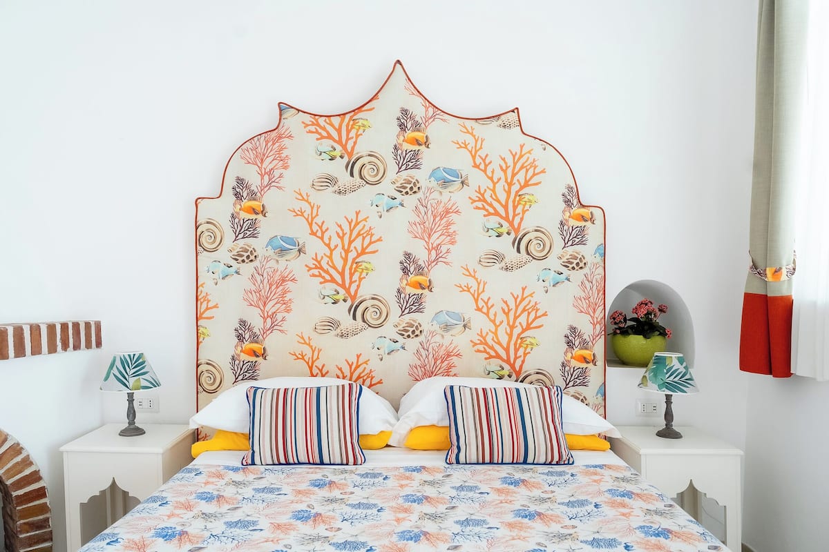 A bedroom with a bed, two bedside tables, a nightstand, a decorative headboard, and a wall with a marine-themed wallpaper.