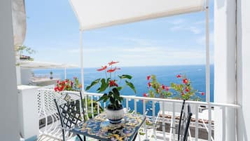 Un balcón con una mesa y sillas, una planta en maceta y vista al mar.