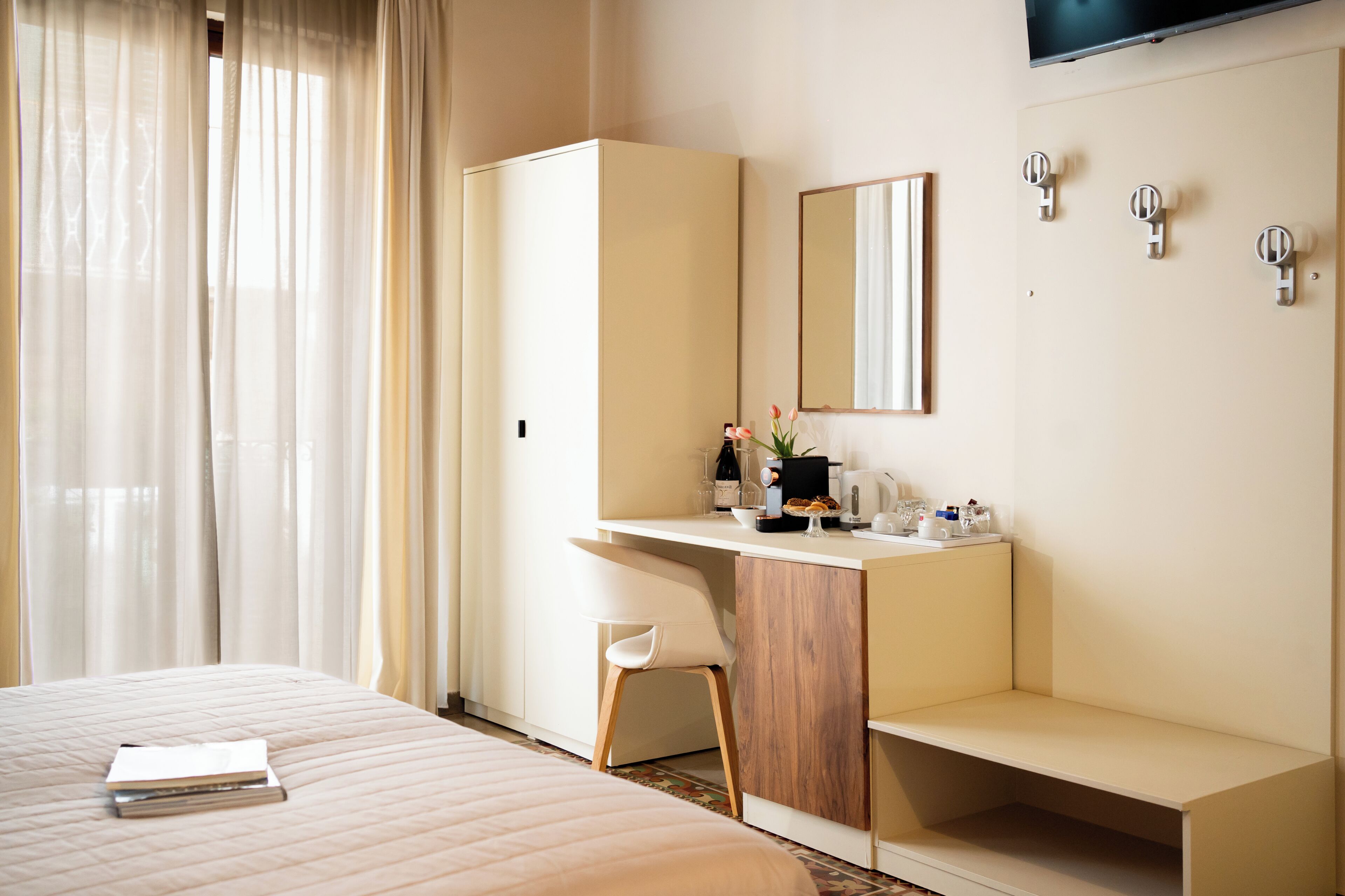 A hotel room with a bed, a desk with a chair, a mirror, and a television.