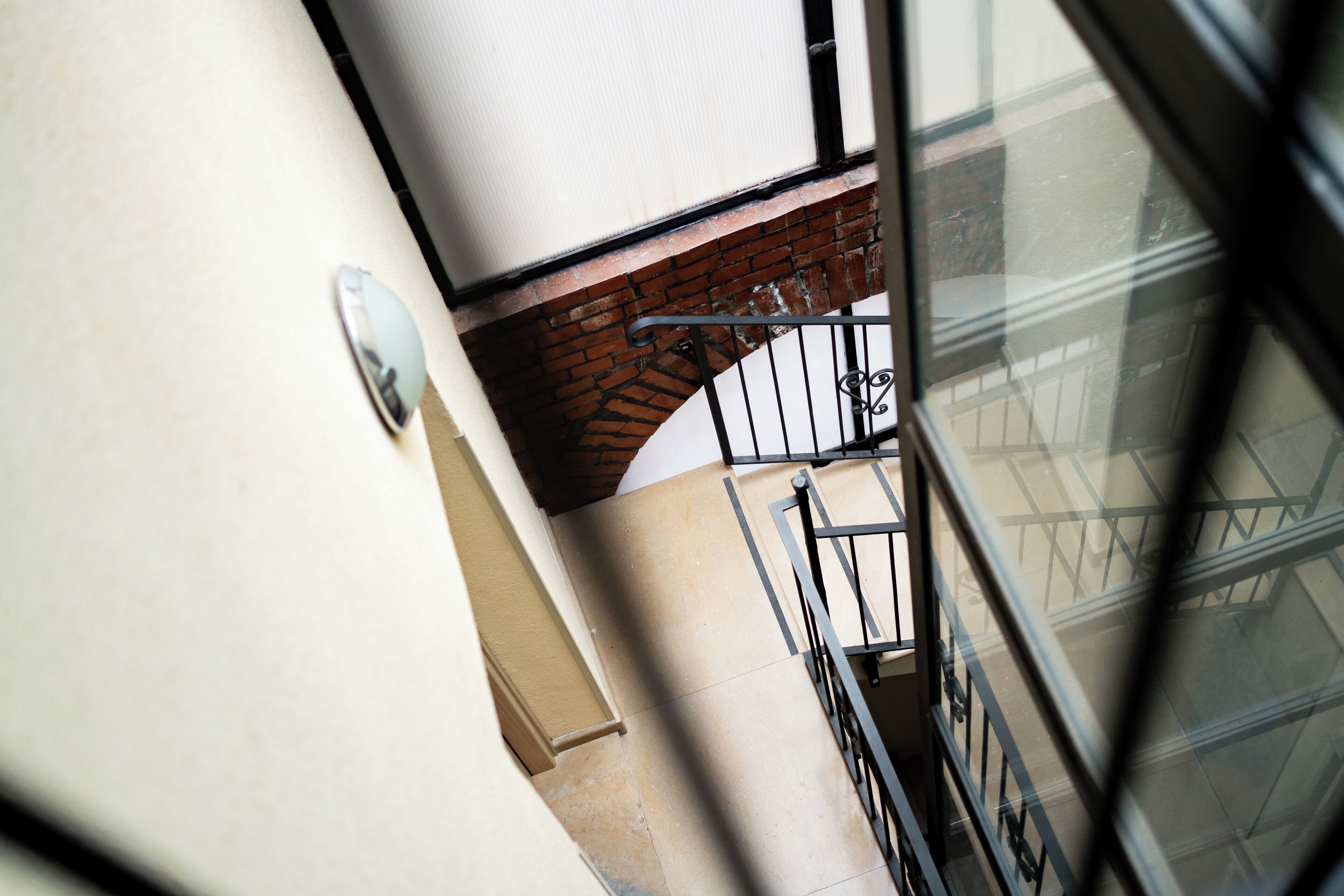 Vista de una escalera con barandilla metálica, pared de ladrillo y un ventanal que refleja la estructura de un edificio.