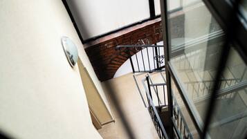 Vista de una escalera con barandilla metálica, pared de ladrillo y un ventanal que refleja la estructura de un edificio.