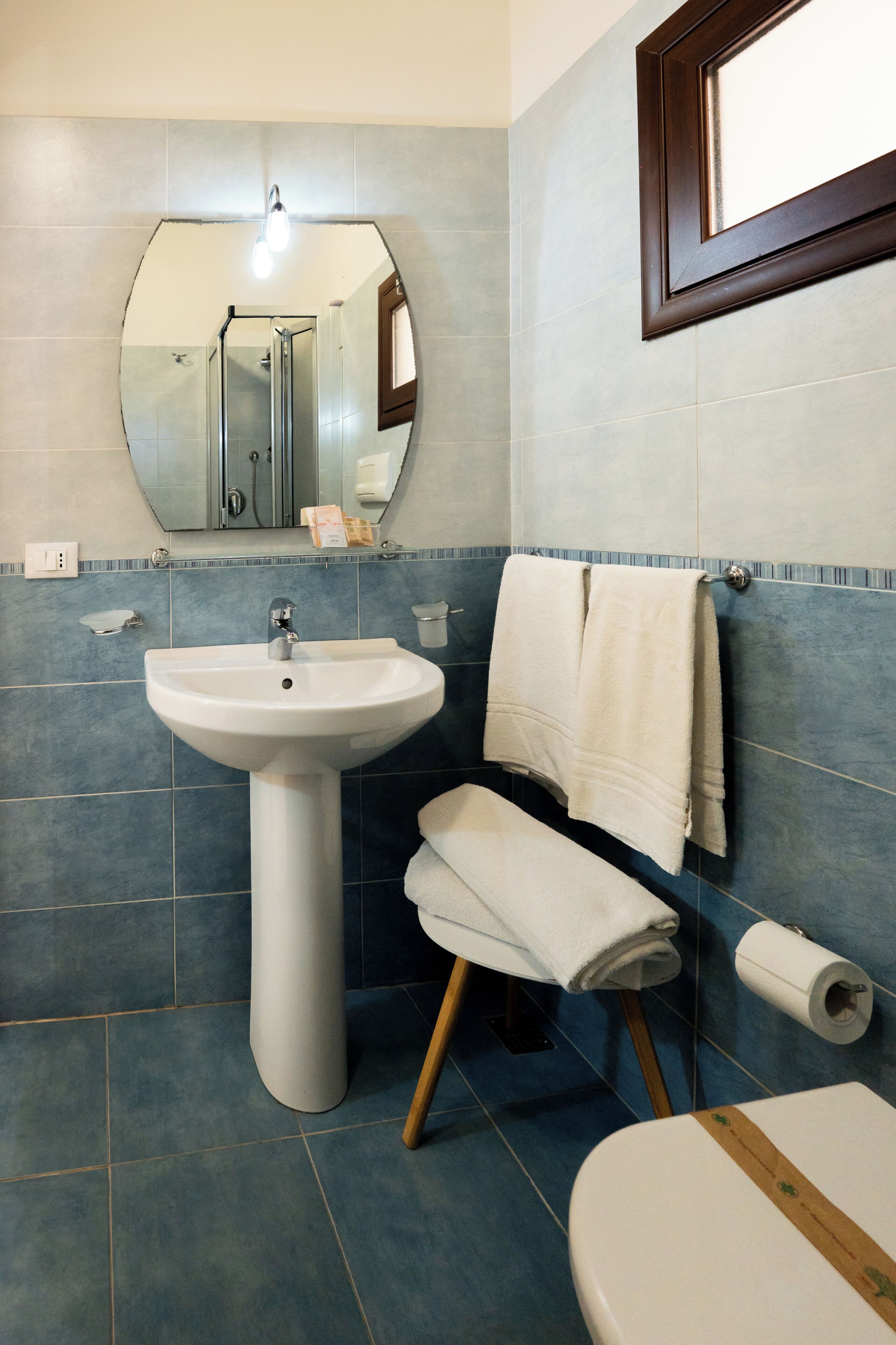 Un baño con lavamanos pedestal, un espejo, toallero, inodoro y dispensador de papel higiénico.