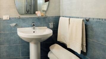 Un baño con lavamanos pedestal, un espejo, toallero, inodoro y dispensador de papel higiénico.