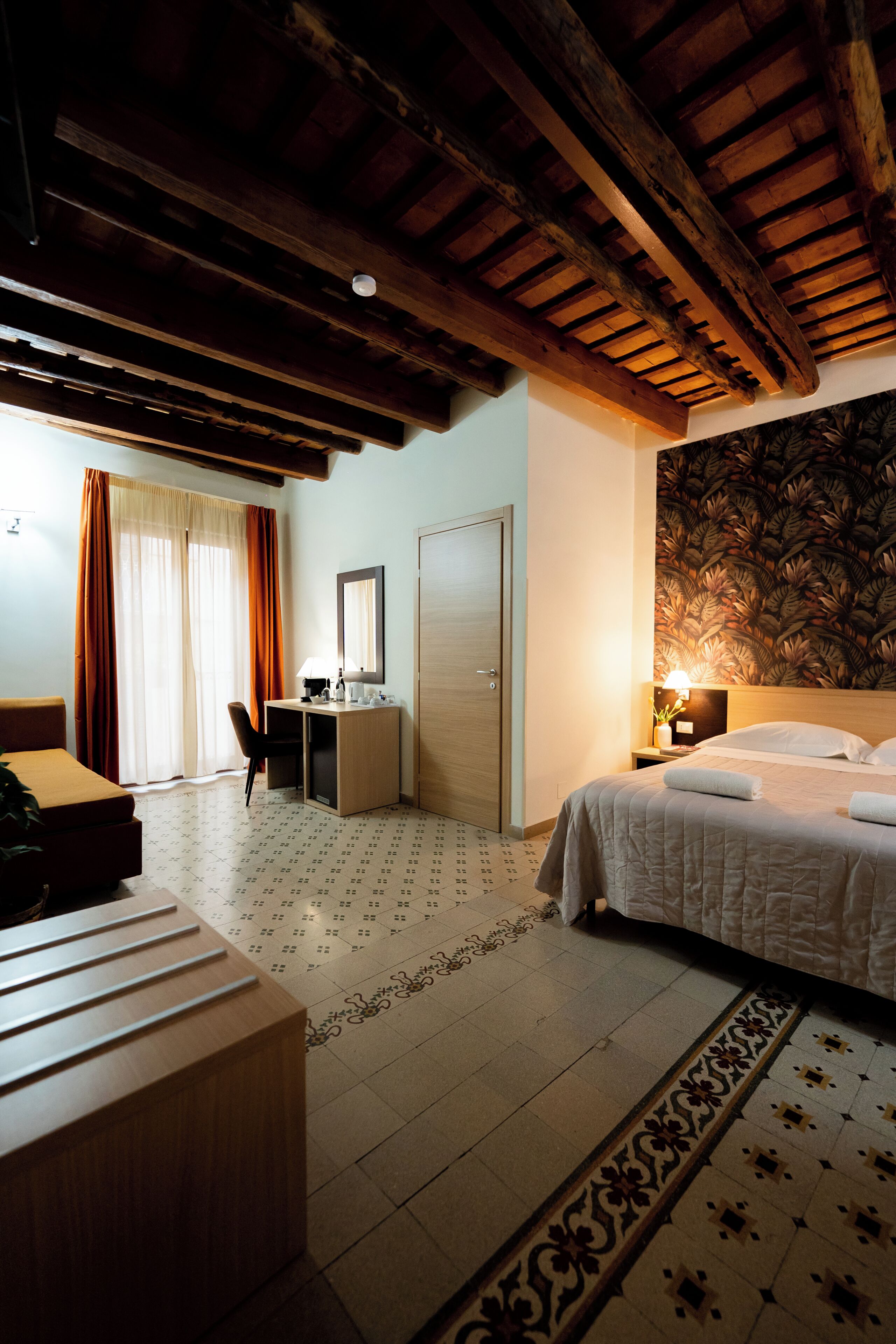 Habitación de hotel con techo de madera, un escritorio con una silla, una cama con cubrecama blanco y una pared con diseño.