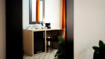 A hotel room with a wooden desk, a mirror, a coffee maker, a chair, and a potted plant.