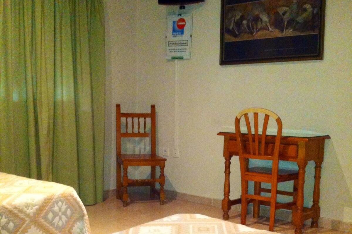 A room with a bed, a chair, a desk, a television, and a painting on the wall.