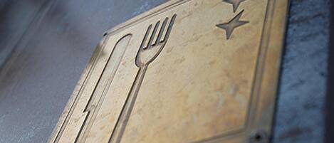 A metal plaque with a fork and spoon symbol, indicating a dining area.
