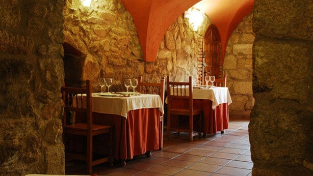 A stone-walled dining area with tables set for two, each with a red tablecloth and wine glasses. - Hostal León (Trujillo)