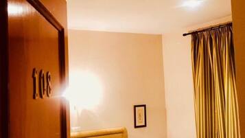 Una habitación con dos camas, una puerta de madera, un cuadro en la pared y una cortina.