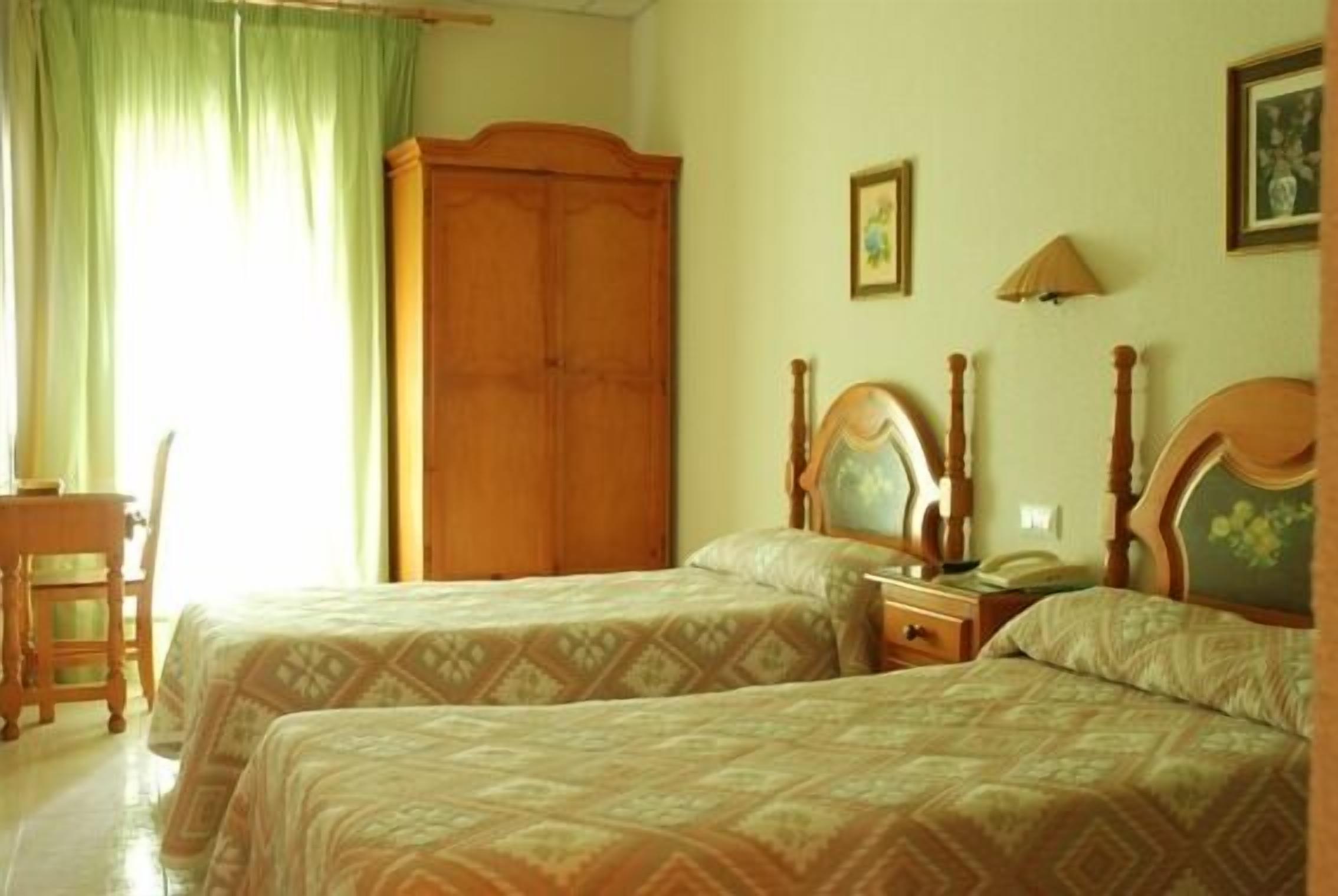 Una habitación con dos camas, un armario de madera, un escritorio y una silla.