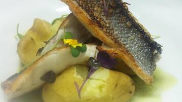 A plate with a grilled fish, potatoes, and a sauce.