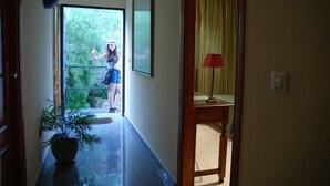 A hallway with a potted plant, a glass door leading outside, and a red lamp on a table. - Hostal León (Trujillo)