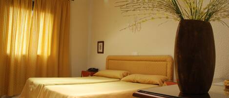A hotel room with two beds, a large vase with flowers, and a nightstand with a phone.