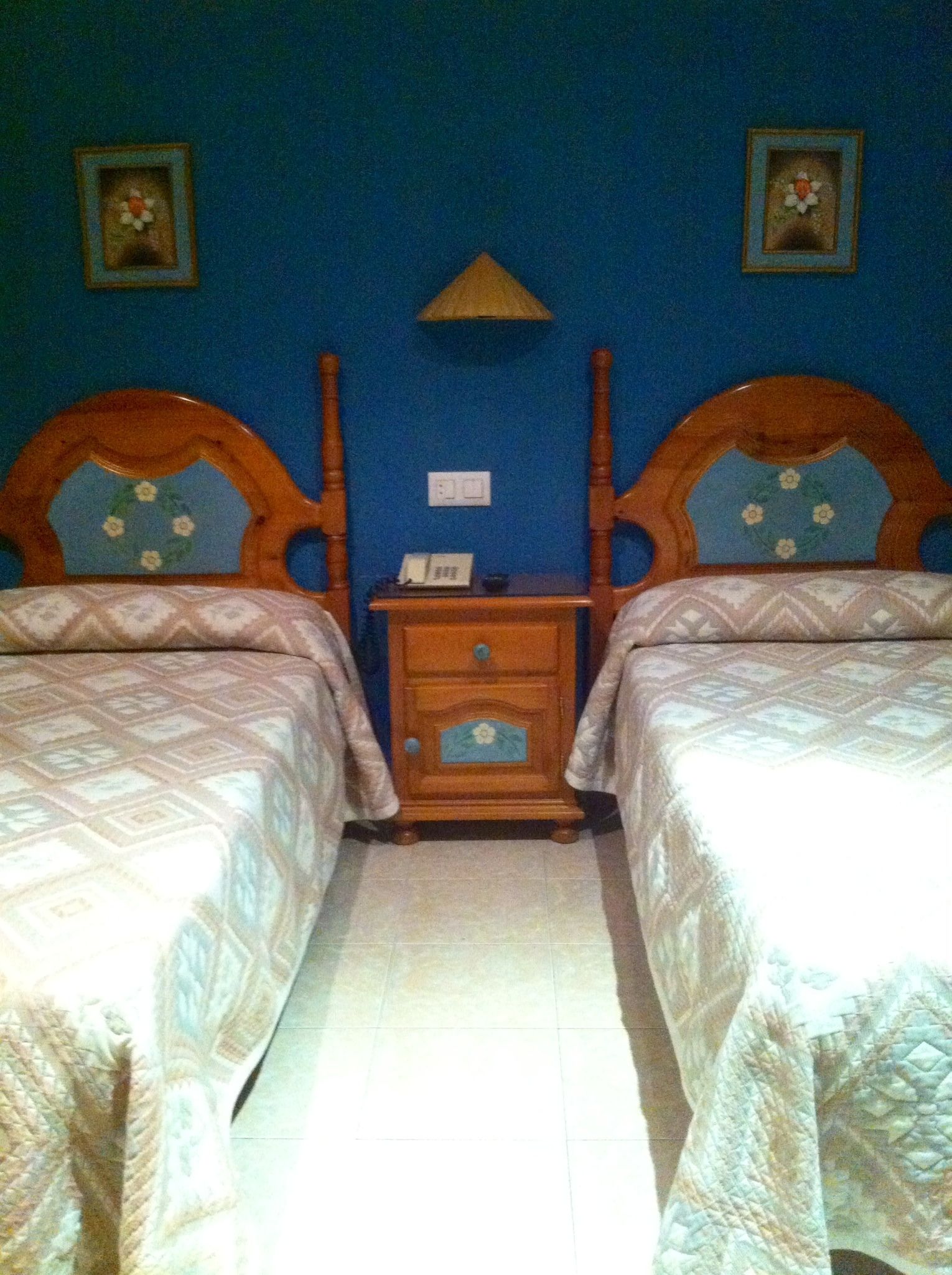 Una habitación con dos camas, una mesita de noche y una lámpara fijada a la pared.