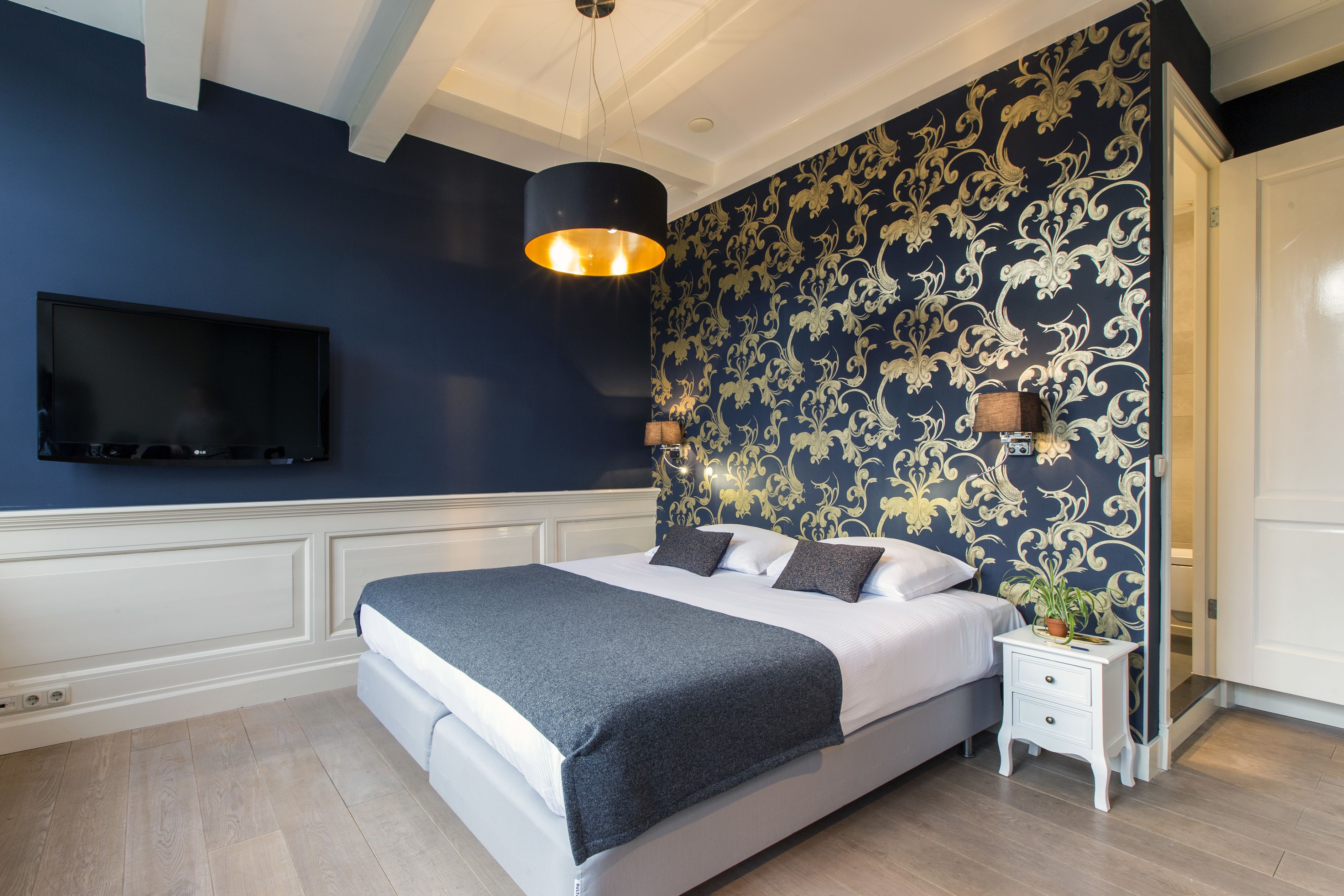 Een slaapkamer met een bed, nachtkastje, lamp en een tv aan de muur.