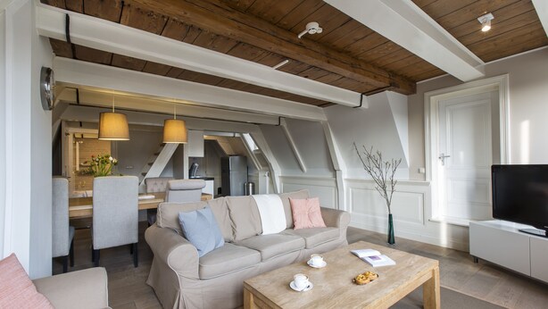 Una sala de estar moderna con un sofá, una mesa de centro y un televisor. En el fondo, hay un comedor con sillas y una mesa.