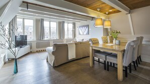 Una sala de estar moderna con techo de madera, un sofá color beige, una mesa de comedor con sillas y un ventanal con cortinas.
