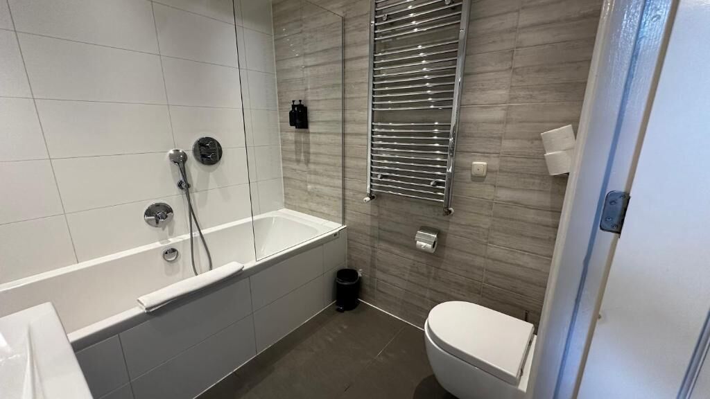 A modern bathroom with a bathtub, toilet, and a glass shower enclosure.