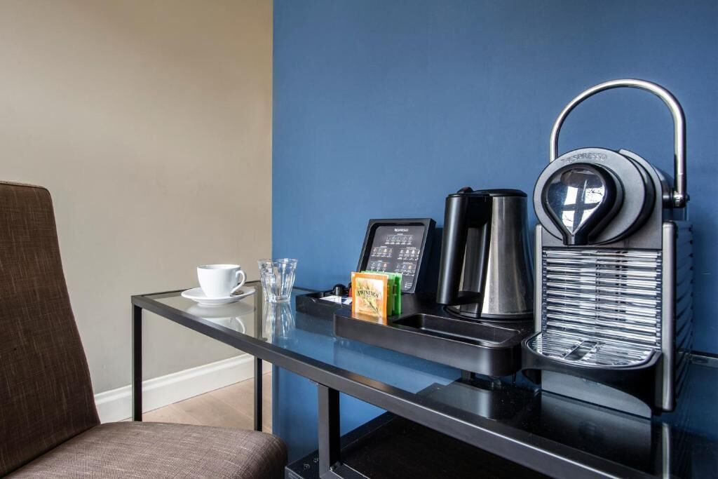 A compact room with a glass table, a coffee machine, a kettle, and a cup of coffee.