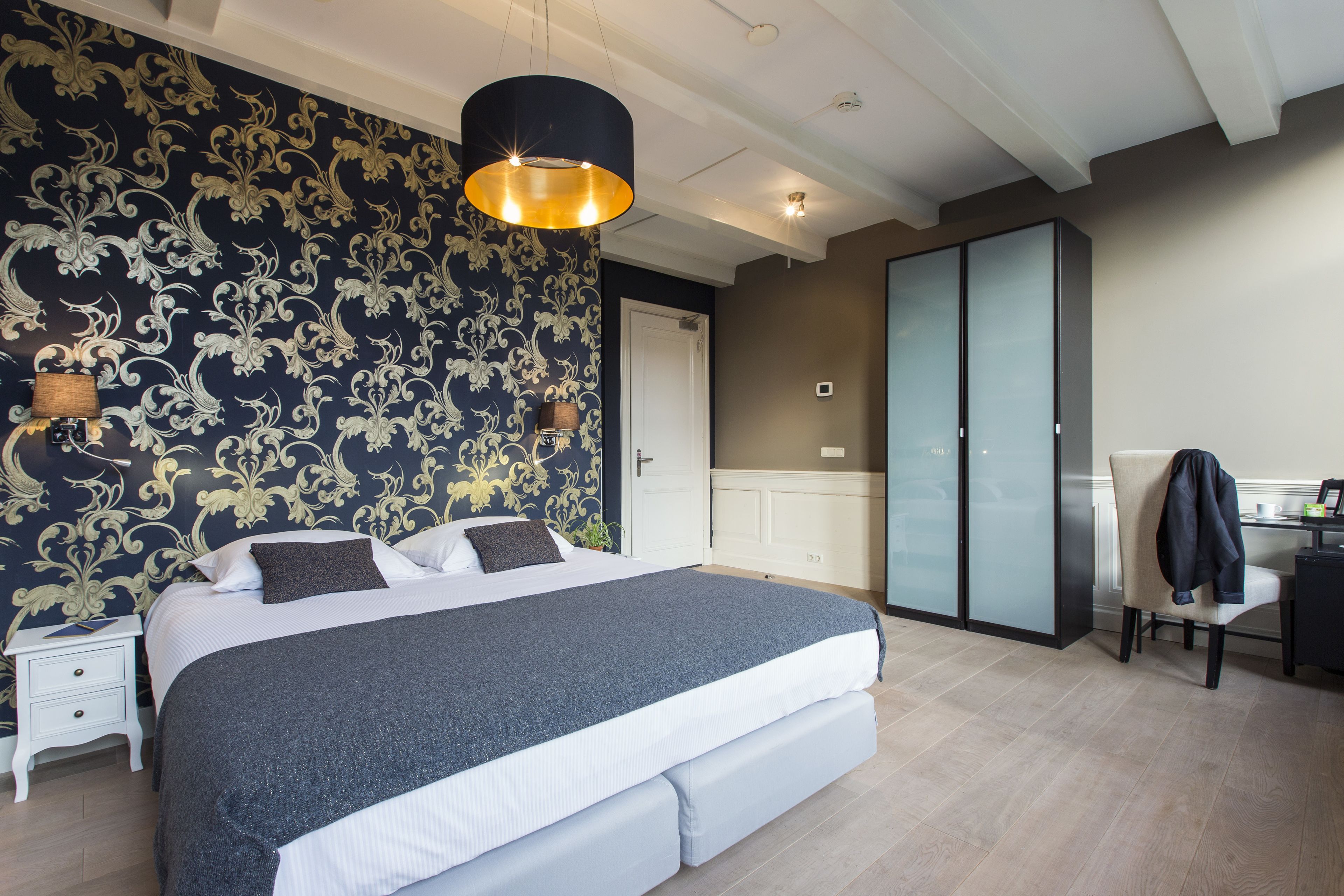 A bedroom with a large bed, a nightstand, a desk, a chair, and a wardrobe.