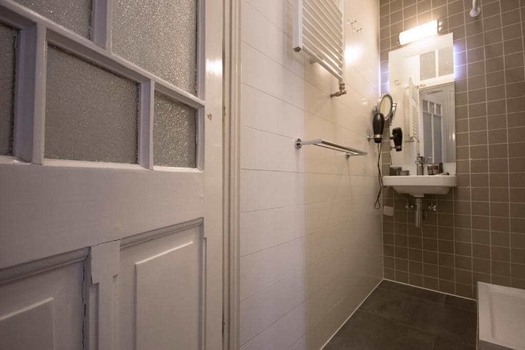 Une salle de bain avec une porte blanche, des fenêtres en verre dépoli, un porte-serviettes, un lavabo et un miroir.